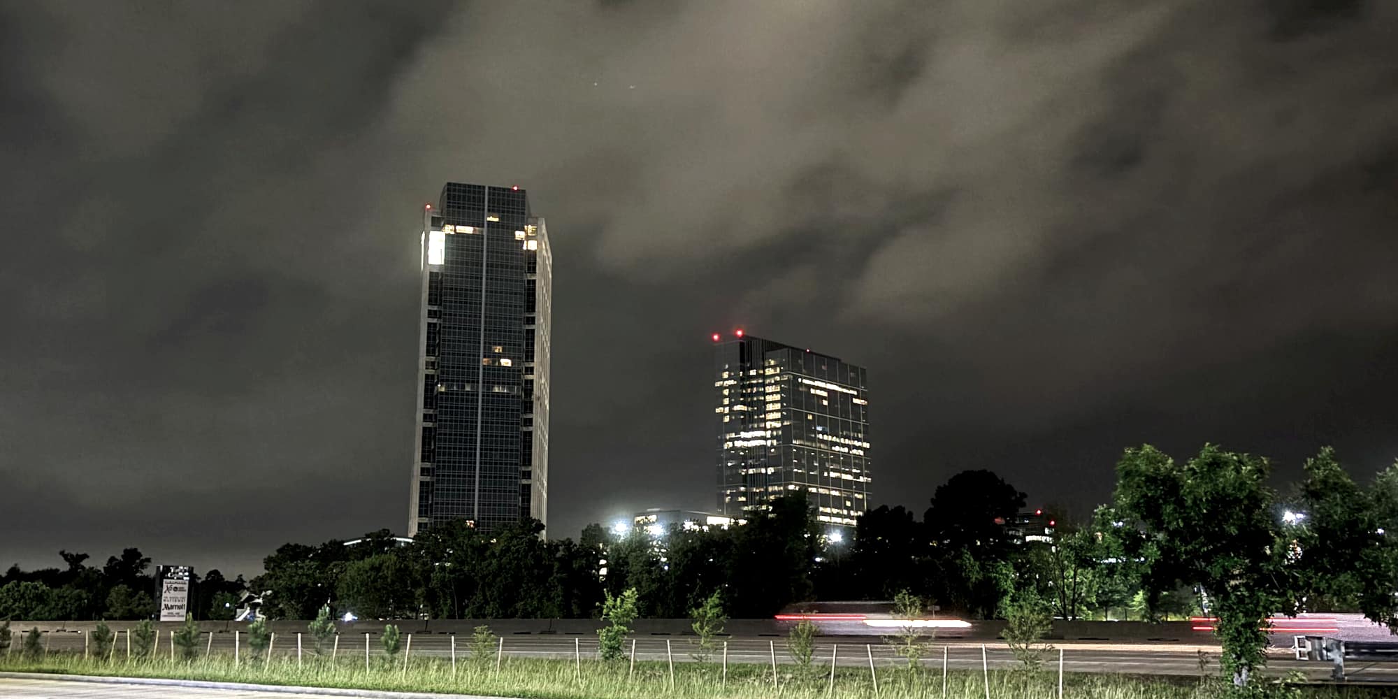 Office towers rising above the trees in The Woodlands at night